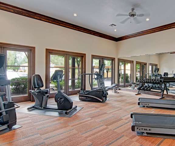 A spacious gym with cardio machines, windows, TVs, and weights at Retreat at Speedway Apartment Homes. 