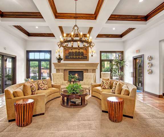 The amazing resident lounge with a fireplace, golden couches, decorations, large windows, a chandelier, plush golden chairs, and coffee tables at the Retreat at Speedway Apartment Homes. 