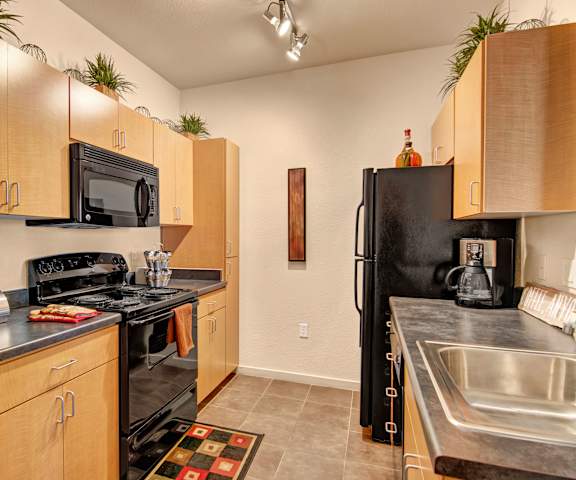 A spacious kitchen with black appliances, dark countertops with lots of room, and wooden cabinets with decorations at Visions Apartment Homes. 