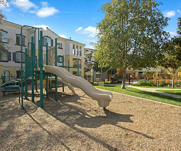 A fun playground at a park with trees and grassy area by the apartments at Fresco. 