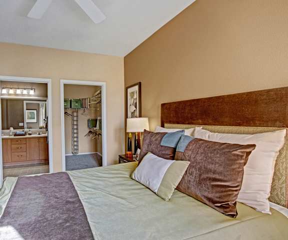 A bedroom with a green and brown king-size bed, walk-in closet, en suite bathroom, and nightstands at Fresco. 