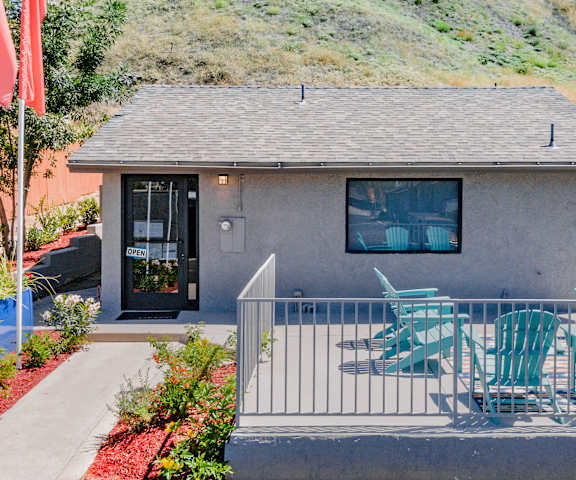 The exterior of the office with plants in front as well as turquoise chairs in front at Hillside Village Apartments. 