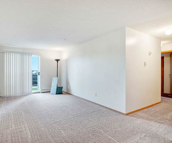 An empty living room with carpeting and a door to the balcony at Edgewood Estates. 
