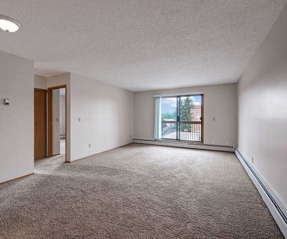 An empty living room with carpeting and a door to the balcony at Gateway Square. 