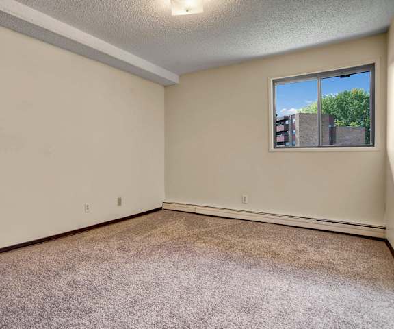 An empty carpeted bedroom with a window at Kingsmere. 