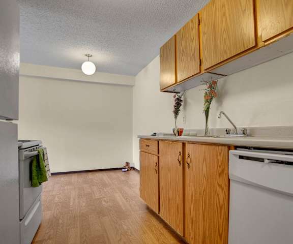 A kitchen with white appliances, light counter, and spacious wooden cabinets at Kingsmere. 