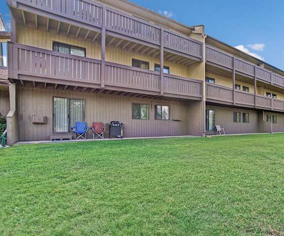 The exterior of the apartments and the green space with grass, trees, and shrubs at Kingsmere. 