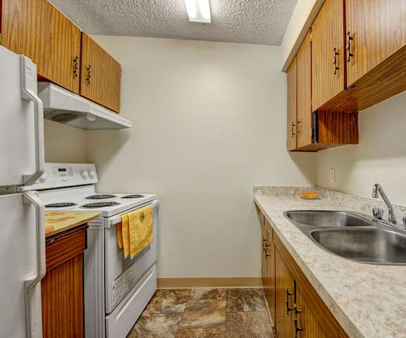 A kitchen with white appliances, light counter, and spacious wooden cabinets at Lakewood Heights. 