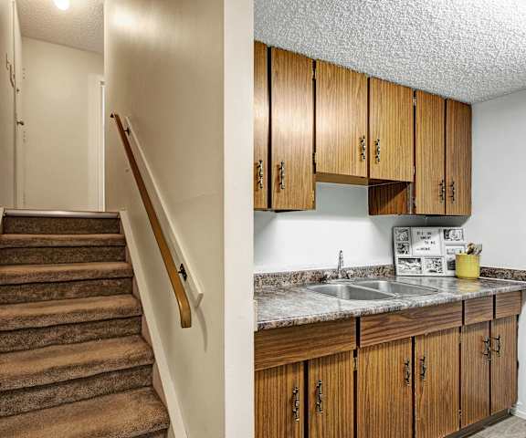 The kitchen with large wooden cabinets and marble counters next to a carpeted staircase at Lakewood Heights. 