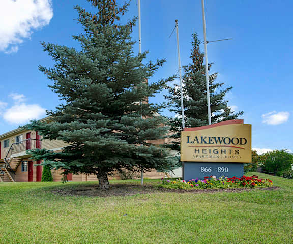 The exterior of the apartments with the entrance sign surrounded by green space with grass, trees, and shrubs at Lakewood Heights. 