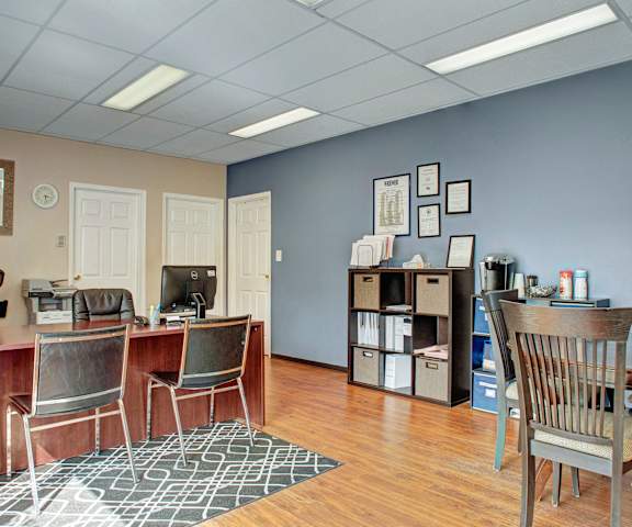 The front office with desks, plush chairs, a bookshelf, desktop computers, table and chairs, and coffee station at Madison Park Apartments.  