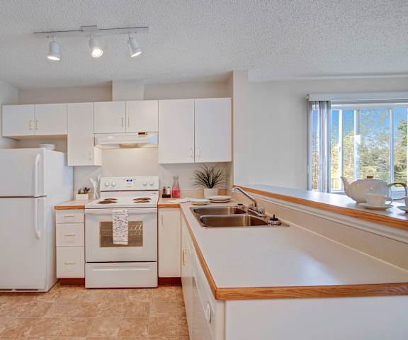 A large kitchen with white appliances, light counter with ample space, and spacious wooden cabinets at Manning Crossing Apartment Homes.