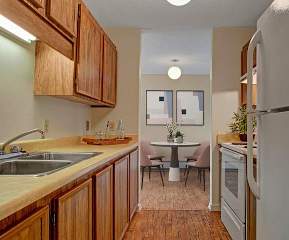 A cozy/large kitchen with white appliances, a light counter with lots of room, spacious wooden cabinets, and a view of the dining room at Ranchlands Apartment Homes. 