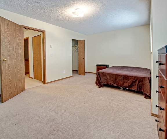 A spacious bedroom with a queen-size bed, a dresser, decorations, closet, and nightstands at Ridgeview Village Apartment Homes. 