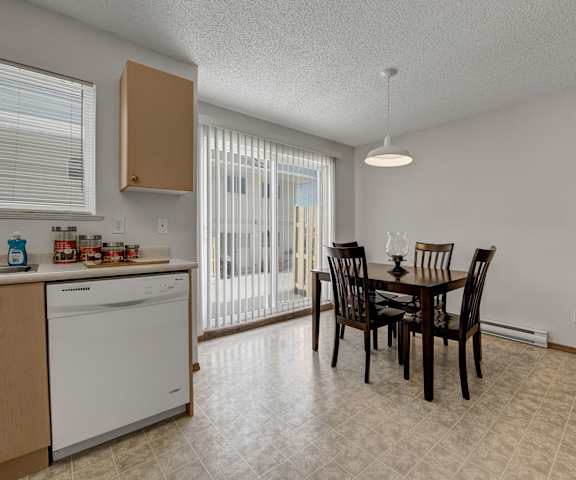 The cozy dining room with a dining table and chairs and a view of the kitchen with light counters, light cabinets, and white appliances at Ridgeview Village Apartment Homes. 