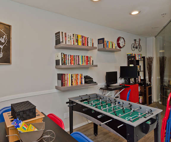 The resident lounge with a game table, a foosball table, bookshelves mounted on the wall with tons of books, two desktop computers, and a bookshelf in the corner at Somerset Pointe Apartment Homes. 