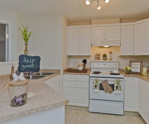 A spacious kitchen with white appliances, kitchen utensils, overhead lighting, light countertops with lots of room, and large white wooden cabinets at Somerset Pointe Apartment Homes. 