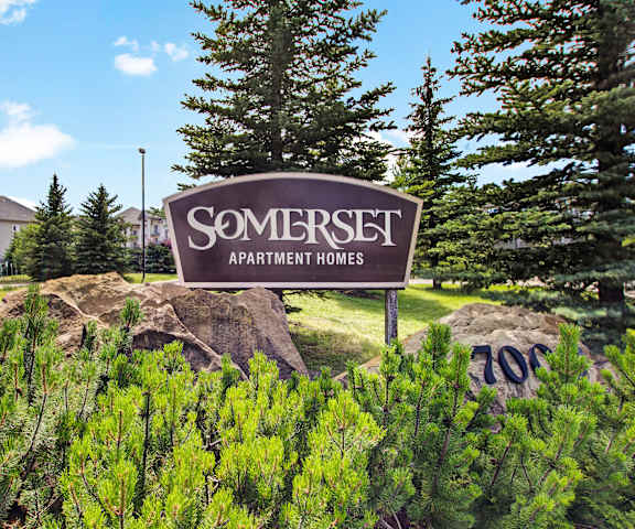 The exterior sign with trees and surrounded by greenery and trees with the buildings in the background of Somerset Pointe Apartment Homes. 
