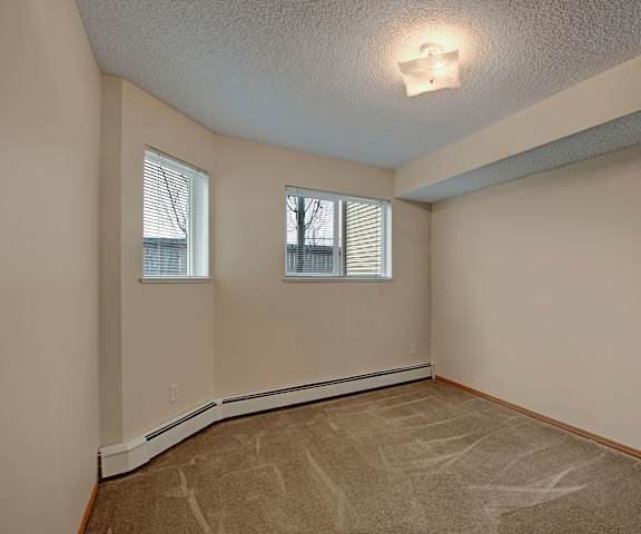 A large, empty carpeted bedroom with overhead lighting and two windows at Sonora Apartment Homes. 