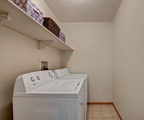 The laundry room with shelves that have storage baskets, a white washer, and a white dryer at Sonora Apartment Homes. 