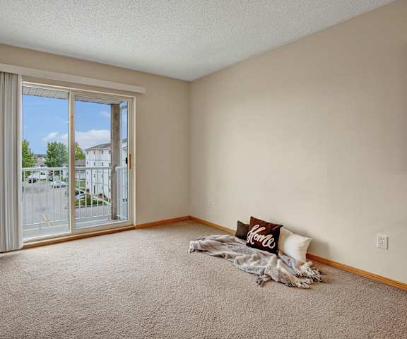 A room with a carpet floor and a window with a view of a parking lot and buildings outside at Westhaven Apartment Homes. 