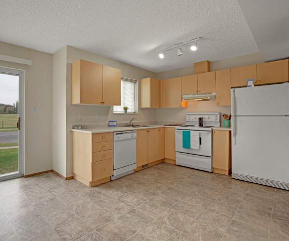 A spacious kitchen with white appliances, overhead lighting, light counter, large wooden cabinets, and the doors the patio at Westhaven Estates Apartment Homes. 