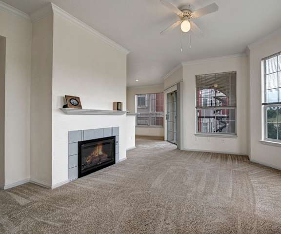 An empty living room with a fireplace and a ceiling fan at Camelback Pointe Apartments. 