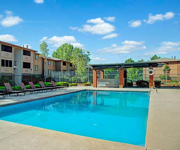 The large, turquoise outdoor pool with pool chairs, tables, and chairs with the apartments in the background at Retreat at Austin Bluffs Apartment Homes. 