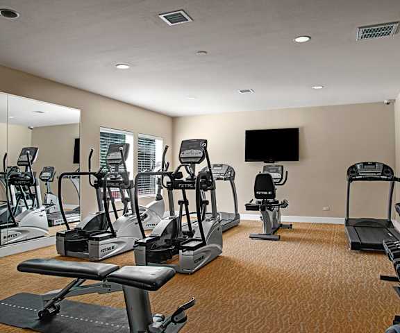 A spacious gym with cardio machines, windows, TVs, and weights at Retreat at Austin Bluffs Apartment Homes. 