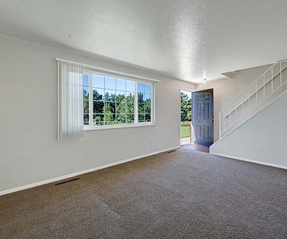 The empty carpeted front entrance room with a closet, stairs to the upstairs, and a large window at Yorkshire Square Apartment Homes. 