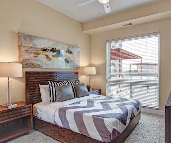 A bedroom at 4800 Excelsior with a bed, nightstands, dresser, and large window. 