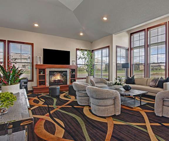 The amazing resident lounge with a fireplace, gray couches, decorations, large windows, gray plush chairs, and coffee tables at the Club at Heritage Apartment Homes. 