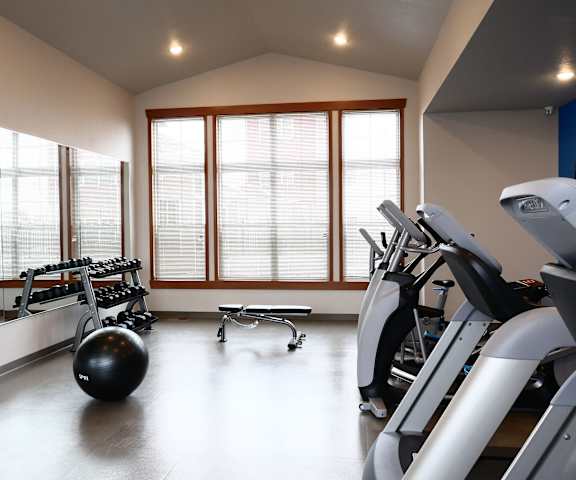 A spacious gym with cardio machines, windows, TVs, and weights at the Club at Heritage Apartment Homes. 
