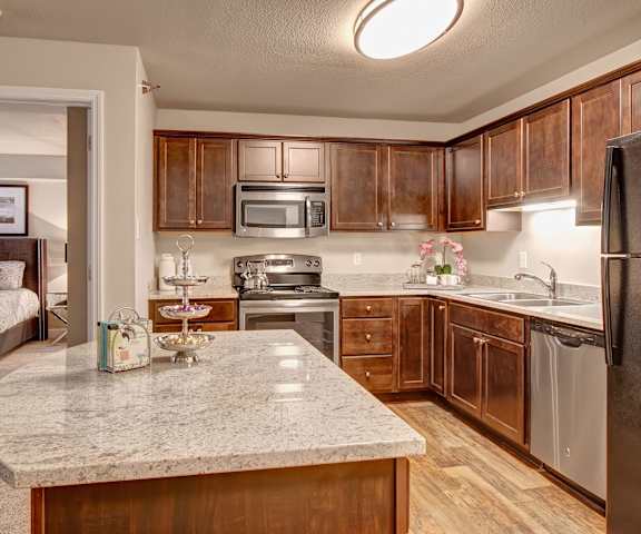 A large, modern kitchen with stainless steel appliances, kitchen utensils, marble countertops with lots of room, a large kitchen island, and large wooden cabinets at Fairways Apartment Homes. 