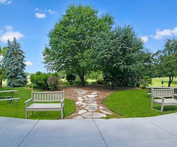 A green space with a stone path flanked by benches leading to a small, wooded area at the Fairways Apartment Homes. 