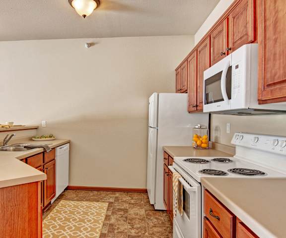 A kitchen with white appliances, light counter, and spacious wooden cabinets at Grand River Estates. 