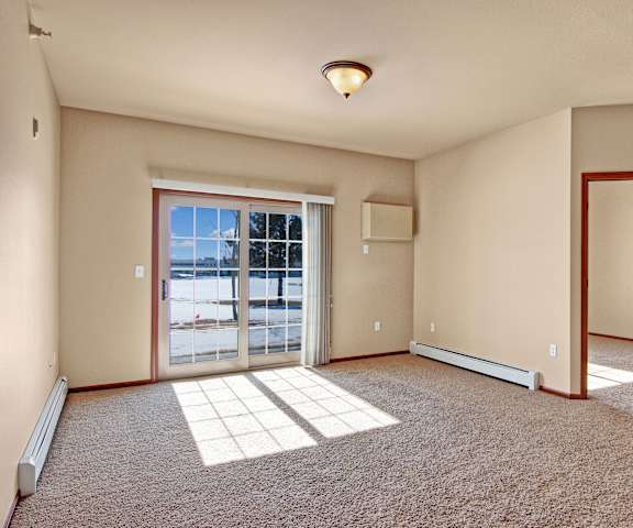 An empty living room with carpeting and a door to the patio at Grand River Estates. 