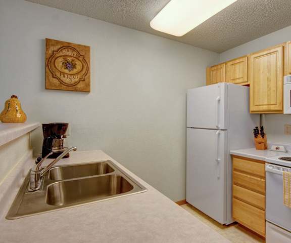 A kitchen with white appliances, light counter, and spacious wooden cabinets at Heritage Park. 