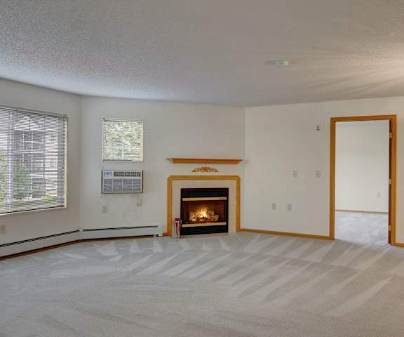 An empty living room with carpeting, windows, and fireplace at Heritage Park. 