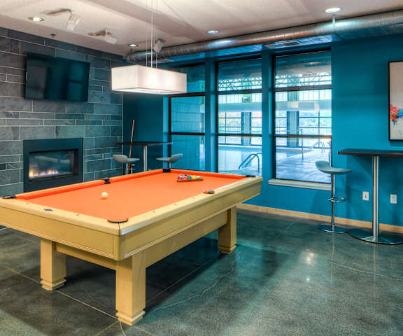 A resident lounge with tables, chairs, fireplace, TV, windows with a view on the indoor swimming pool, and a pool table at Marbella on Dean Apartments. 