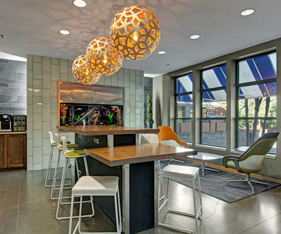 The resident lounge with barstool chairs, tables, stools, decorations, plush chairs, coffee tables, large windows, and French doors to the pool area at Marbella on Dean Apartments. 