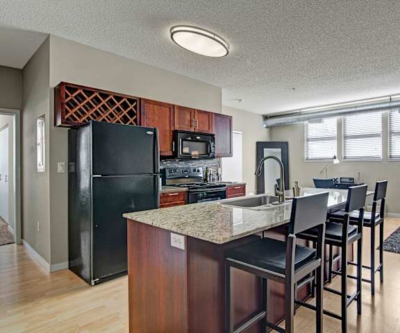 A large kitchen with black appliances, marble countertops with ample space, and spacious wooden cabinets with decorations at Marbella on Dean Apartments. 