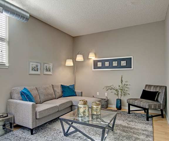 The living room with a window, couch, plush chairs, coffee table, decorations, a TV, and balcony at Marbella on Dean Apartments. 