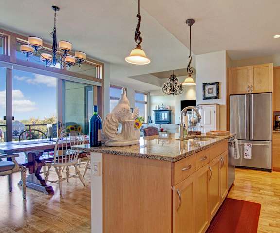 A large, modern kitchen with stainless steel appliances, kitchen utensils, granite countertops with lots of room, a kitchen island, and light, large wooden cabinets at the Mist at Lake Minnetonka Apartment Homes. 