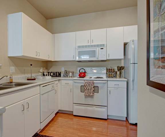 The spacious, all-white kitchen with white cabinets, white appliances, and kitchen utensils at Stoneleigh at the Reserve Apartment Homes. 