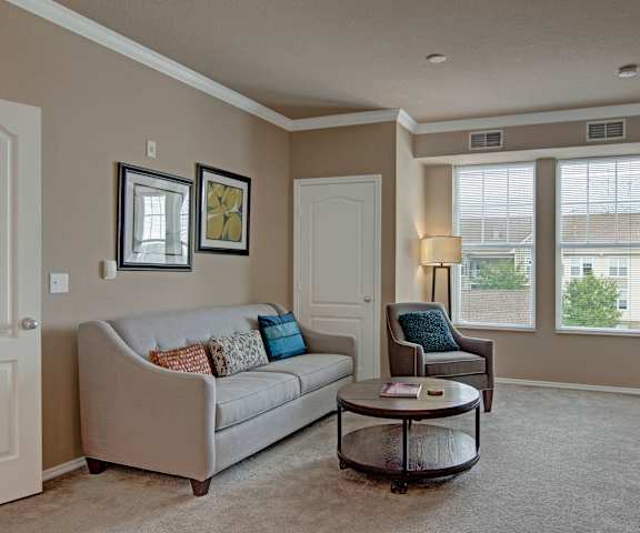 The spacious living room with a white couch, throw pillows, large windows, wall art, a gray plush chair, coffee table, and decorations, at Stoneleigh at the Reserve Apartment Homes. 