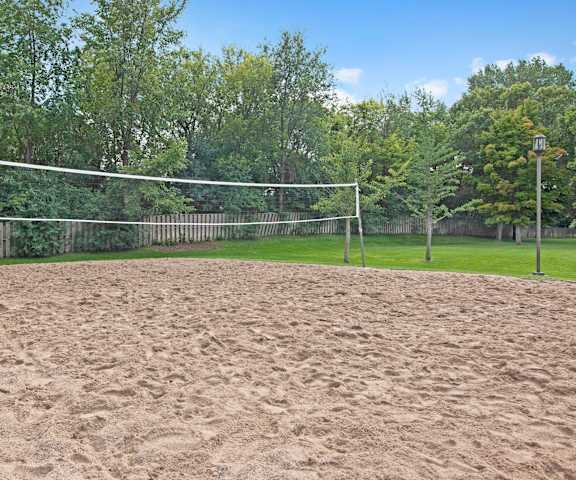 A sandy beach volleyball court with a net and posts with greenery and trees in the background at Town Centre Apartment Homes. 