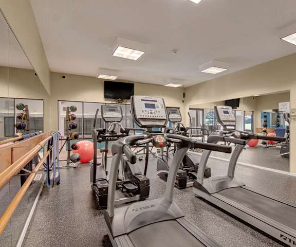 A spacious gym with cardio machines, windows, TVs, and weights at Town Centre Apartment Homes. 