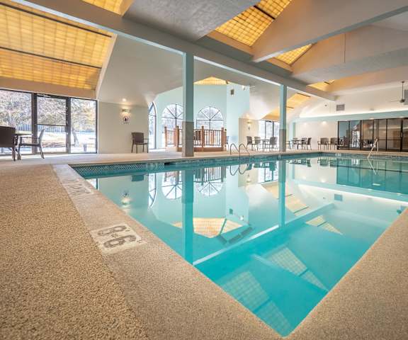 The turquoise indoor pool with tables, chairs, and windows at Town Centre Apartment Homes. 
