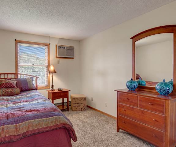 A spacious bedroom with a queen-size bed with a colorful purple, blue, yellow and red bedspread, a dresser, lamp, decorations, and a nightstand at Town Centre Apartment Homes. 